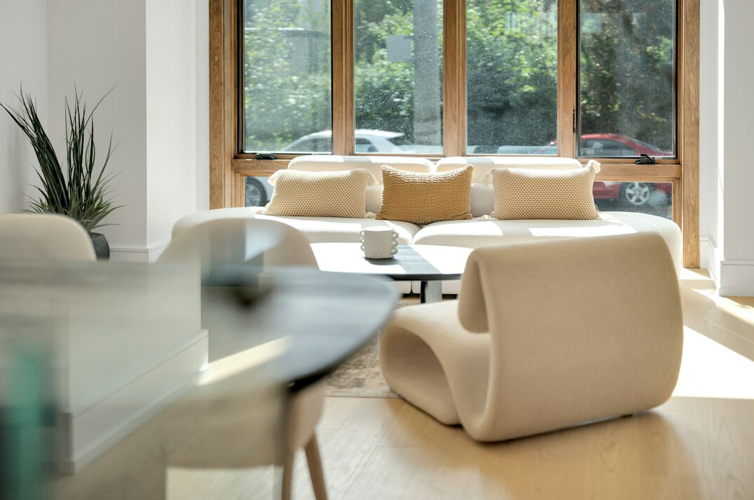 Bright elegant living room with designer sofa, large windows and warm wooden floor